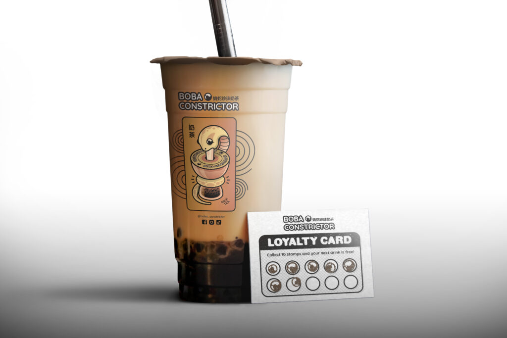 Boba Constrictor cup of milk tea & a customer loyalty card. the Milk Tea flavor illustration is printed onto the side of the clear plastic cup.
